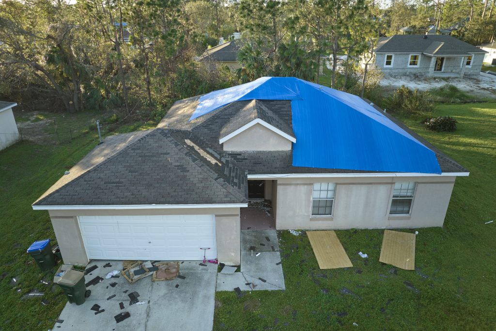 Aerial View Of Damaged In Hurricane Ian House Roof Covered With Blue Protective Tarp Against Rain Water Leaking Until Replacement Of Asphalt Shingles