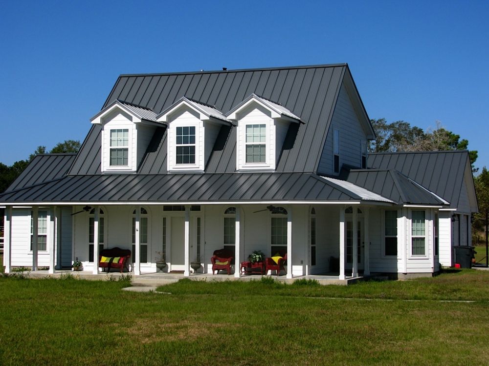 Traditional white house with a gray metal roof featuring dormer windows and a wrap-around porch.