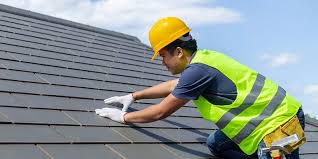 A roofing contractor in a yellow hard hat inspecting roof shingles for damage, ensuring the roof is winter-ready.