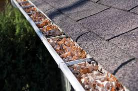 Close-up view of a gutter filled with fallen leaves, highlighting the need for roof and gutter maintenance before winter.