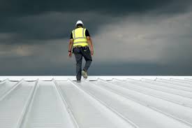 A roofing contractor walking on a white metal roof under a stormy sky, inspecting for potential issues before winter weather.